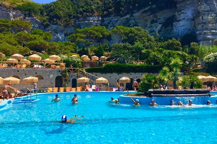 Visitors enjoying a swim in the vibrant blue pool surrounded by greenery at Poseidon Gardens, Ischia.