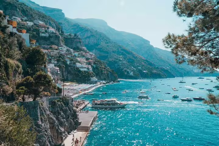Panoramic view of Positano coastline with turquoise water, boats, and cliffside buildings on Amalfi Coast