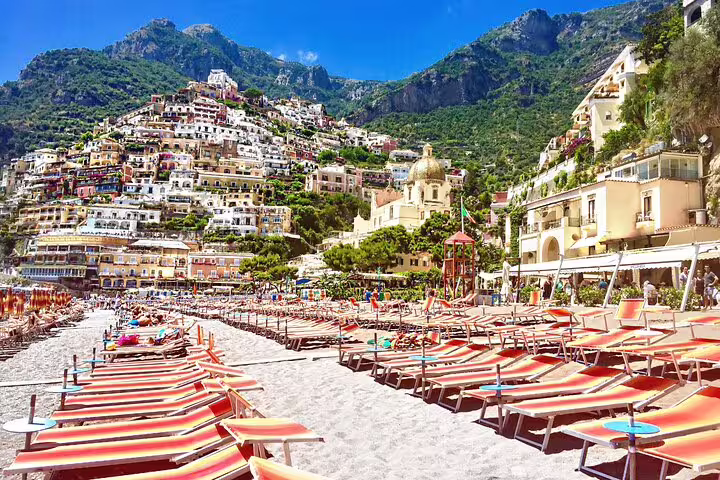Colorful beach loungers on Positano beach with cliffside village and lush mountains on Amalfi Coast