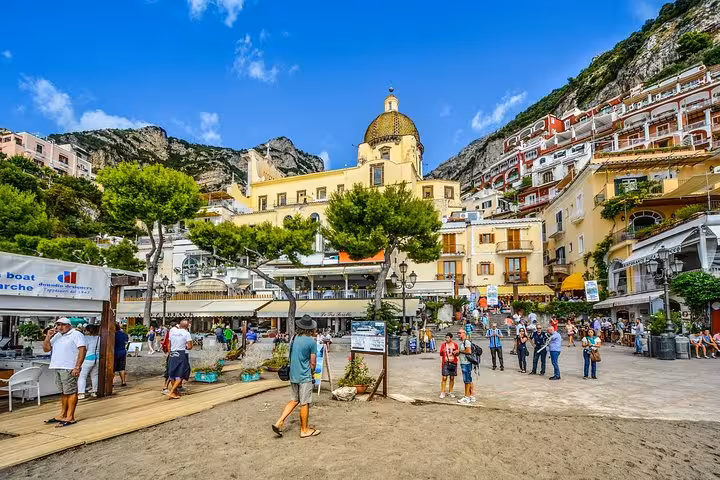Vibrant scene of Positano's bustling beachfront with colorful buildings and the iconic church under a clear blue sky.