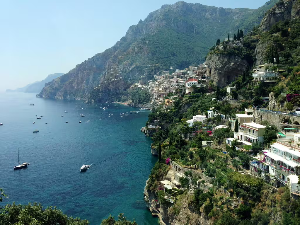 Boats dot the turquoise sea below Positano’s cliffside houses on a scenic Amalfi Coast and Ravello full-day tour