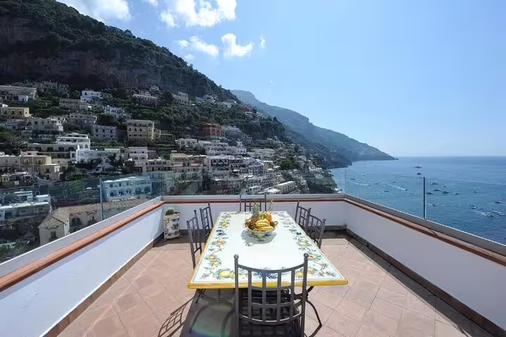 Panoramic terrace with dining table overlooking Positano cliffside village and blue Mediterranean Sea