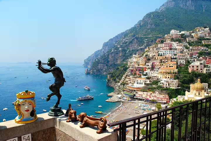 Panoramic view of Positano colorful cliffside village with bronze statue and ceramic figurines in foreground, Amalfi Coast