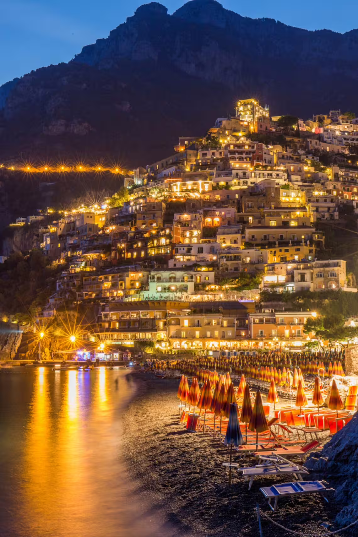 Positano at night with glowing hillside lights and beach umbrellas, From Dusk Till Night immersive experience