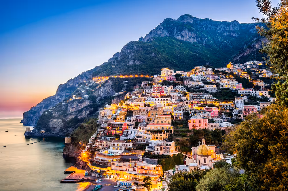 Sunset over Positano on the Amalfi Coast with illuminated hillside houses and serene sea, perfect for a day trip.