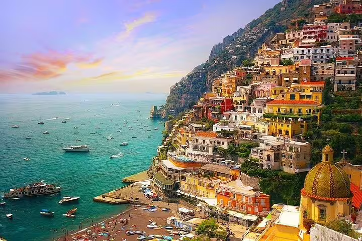 Sunset over Positano’s terraced houses and lively beach dotted with boats on a private full day Amalfi Coast tour