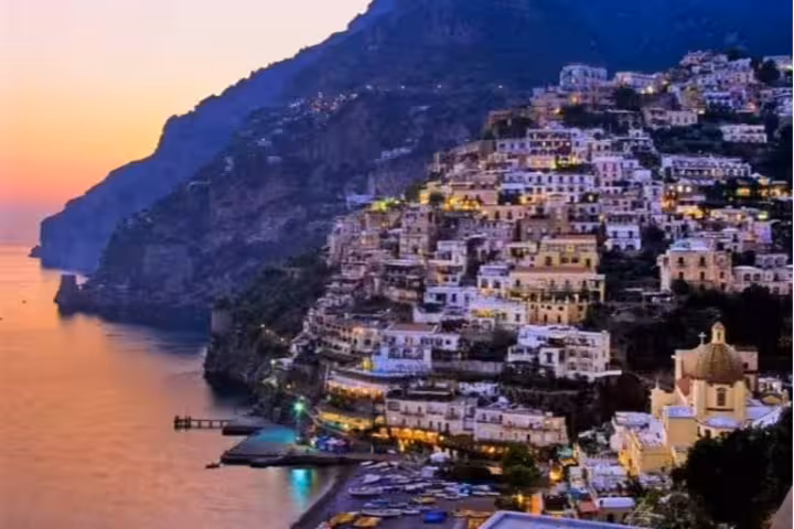 Sunset over Positano’s colorful cliffside houses and Amalfi Coast shoreline, included in a shared Positano and Pompei tour itinerary