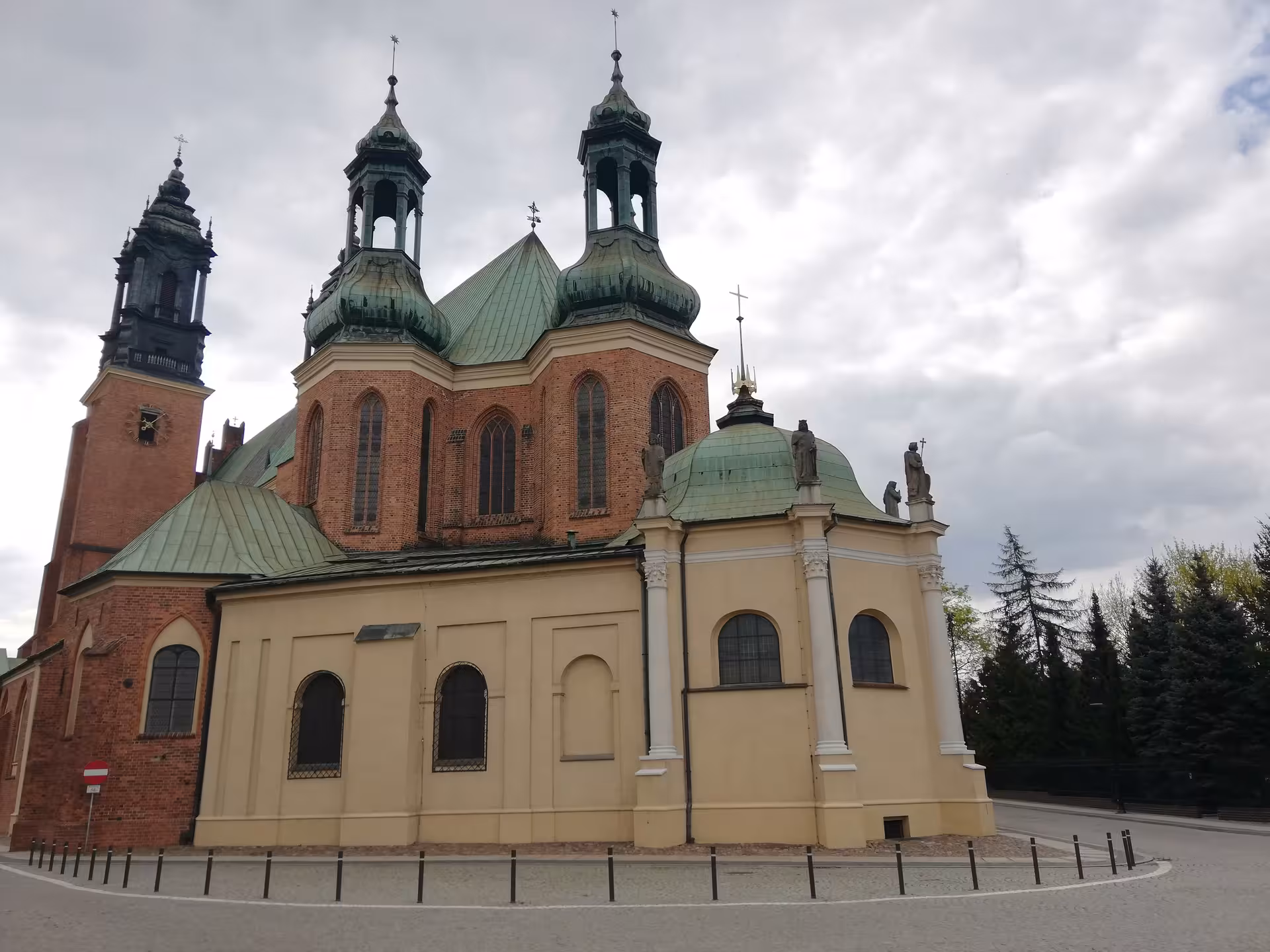 Historic Poznan Cathedral on Ostrow Tumski with green copper domes and brick towers under a cloudy sky