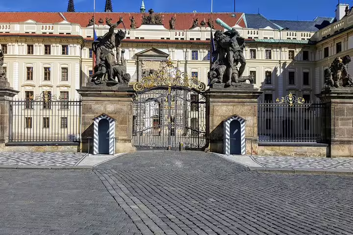 Ornate golden gate entrance to Prague Castle with baroque sculptures and sentry boxes