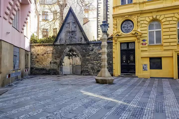 Medieval stone gateway with Gothic arch and ornate yellow building in Prague Old Town cobblestone square