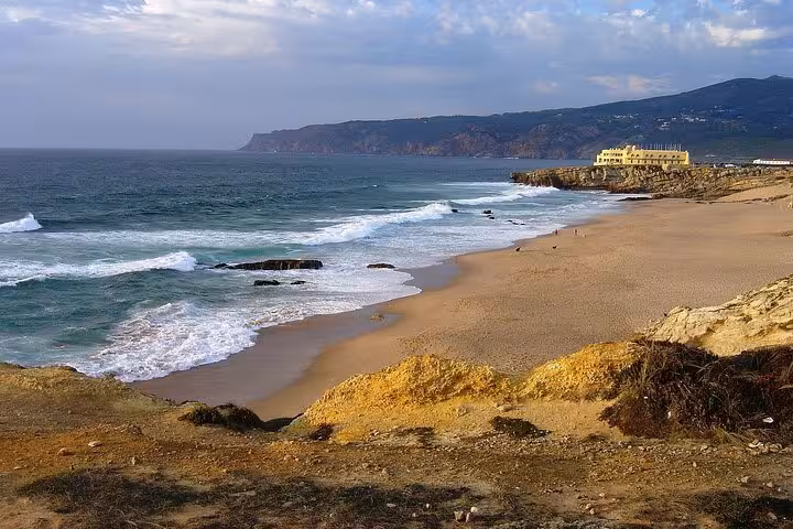 Scenic Praia do Guincho with waves lapping golden sands and coastal cliffs, perfect for a Cascais day trip.