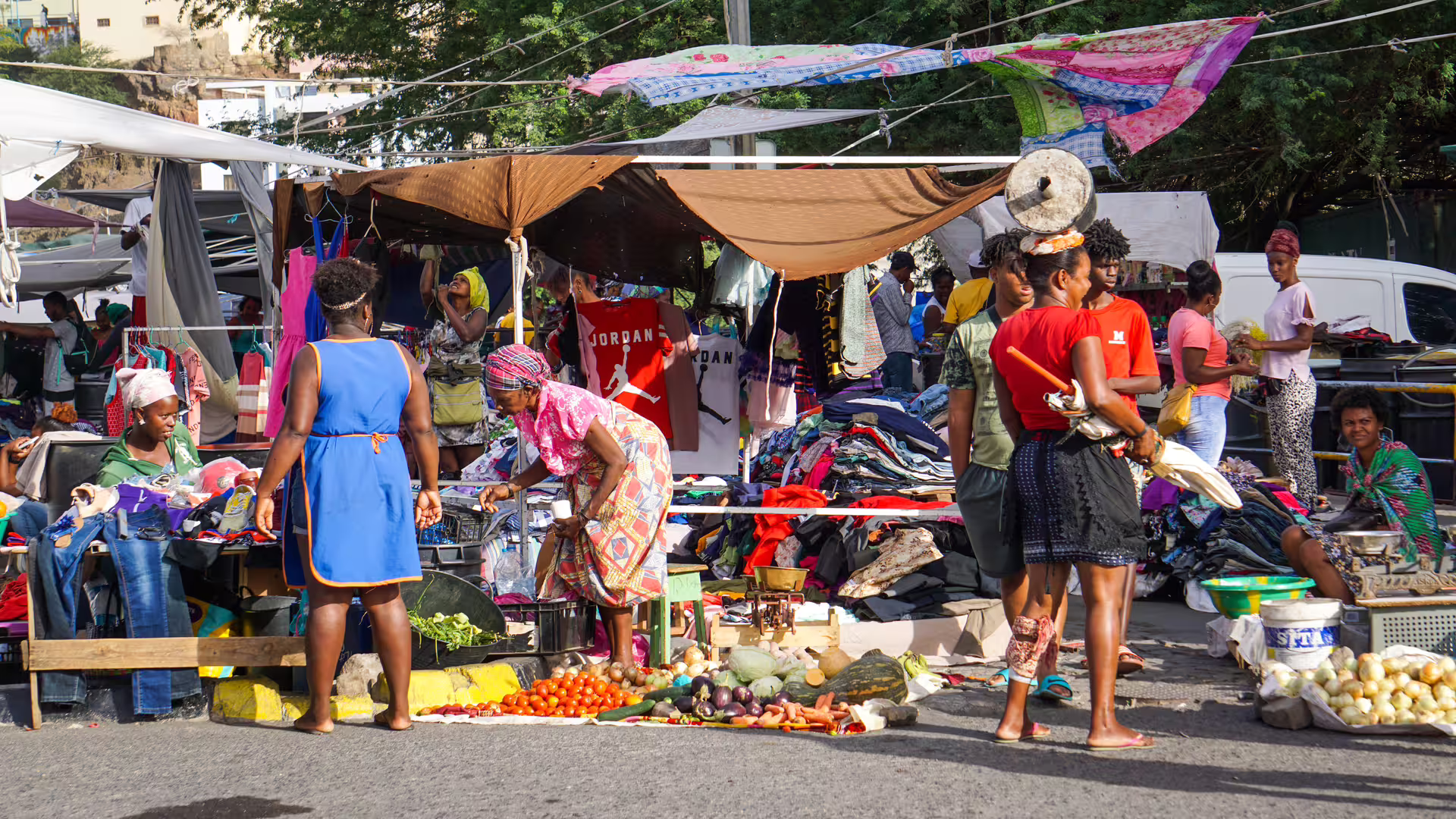 Bustling Praia market scene with locals shopping for fresh produce and clothing on guided historic tour.