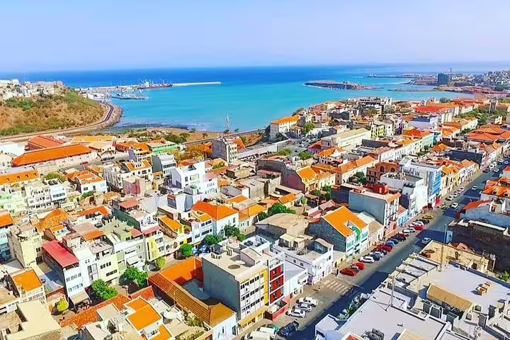 Aerial view of Praia's vibrant cityscape with colorful buildings and a stunning coastline under a clear blue sky.