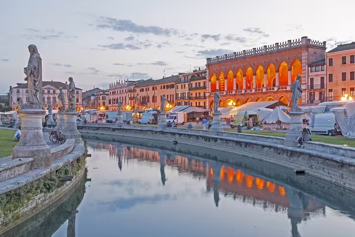 Evening view of Prato della Valle in Padua with statues, market stalls and lit loggia seen on a private guided walking tour