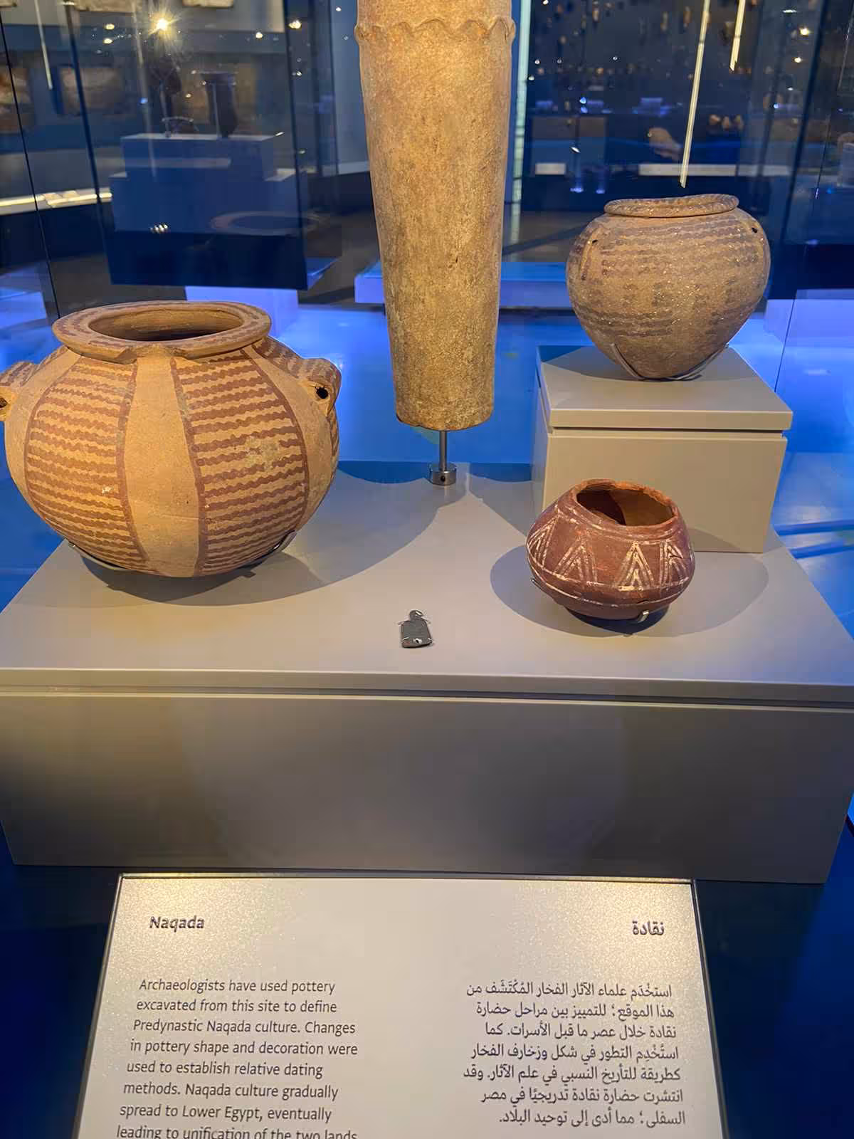Predynastic Naqada pottery display at the Grand Egyptian Museum, featuring painted jars and stone vessels
