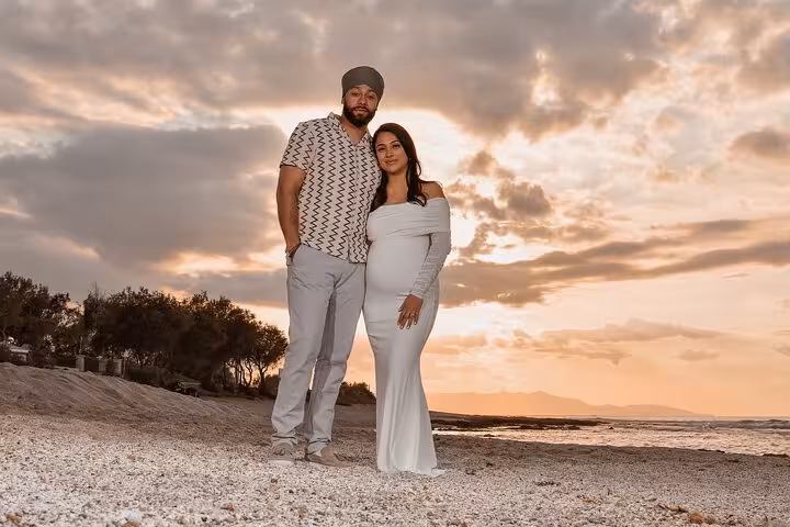 Expectant couple poses on Heraklion beach at sunset, celebrating pregnancy with serene ocean backdrop.
