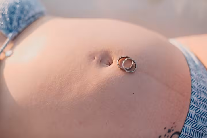 Close-up of a pregnant belly adorned with wedding rings during a Gouves beach photoshoot, symbolizing love and family.