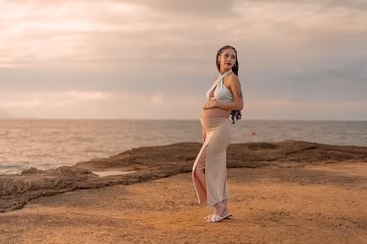 Pregnant woman posing gracefully on a rocky shore in Analipsi, capturing a serene moment during a private photoshoot.