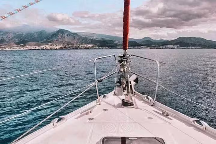 Front view from a premium yacht charter cruising towards scenic coastal mountains under a partly cloudy sky.