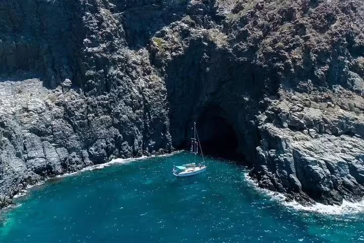 A premium yacht anchored in a serene cove near dramatic rocky cliffs and a sea cave.