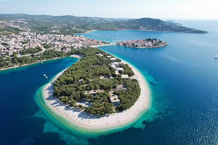 Drone view of Primosten peninsula beach and pine forest, crystal-clear Adriatic bay on a scenic shore excursion