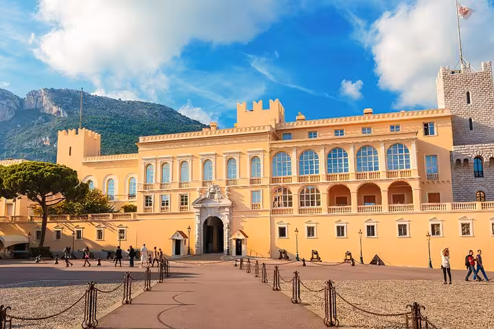The majestic Prince's Palace of Monaco with its grand architecture set against a backdrop of mountains and blue skies.