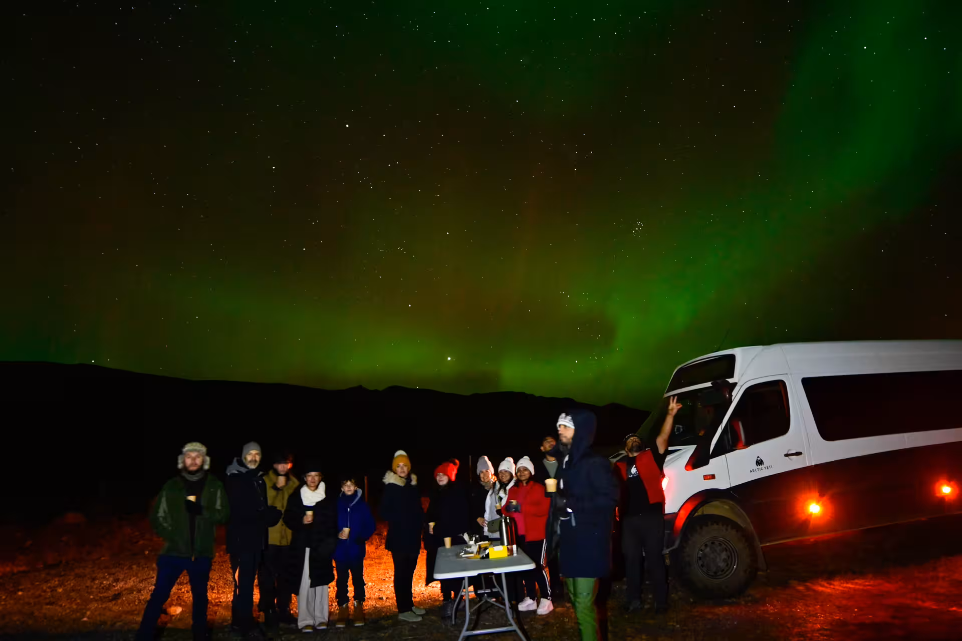 Guests and guide gathered by a 4x4 vehicle under glowing green northern lights on a private aurora tour from Reykjavik
