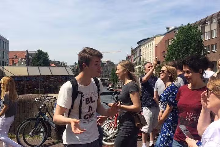 Local guide leading private Amsterdam old city walk by canal, sharing stories near bikes and bridges