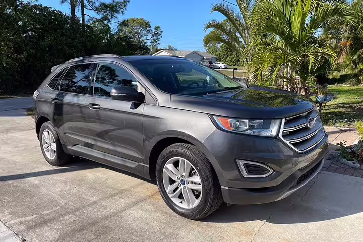 Gray Ford Edge SUV parked on driveway with palm trees in background