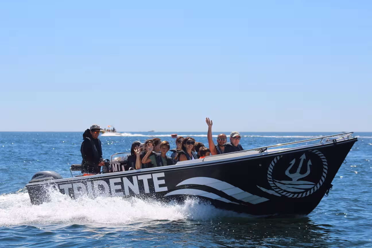 Happy tourists waving aboard Tridente private speedboat cruising the Algarve coast on a deluxe Benagil Cave tour