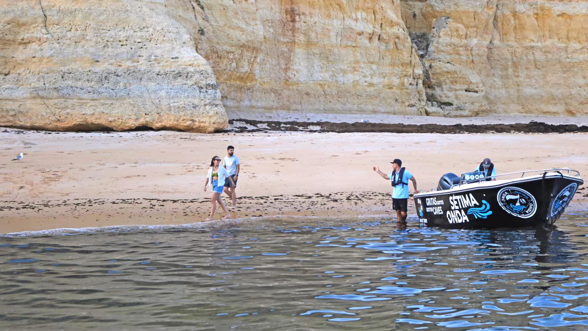 Couple enjoys private Benagil cave tour landing on secluded Algarve beach beside guide and branded speedboat in Portugal