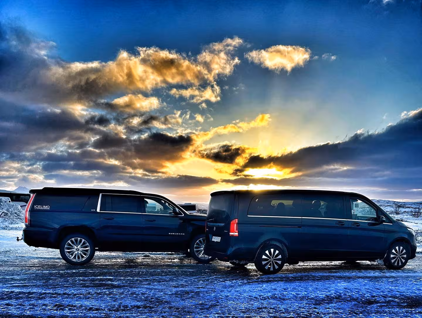 IceLimo black Suburban and VW van parked in snowy Iceland landscape at sunset