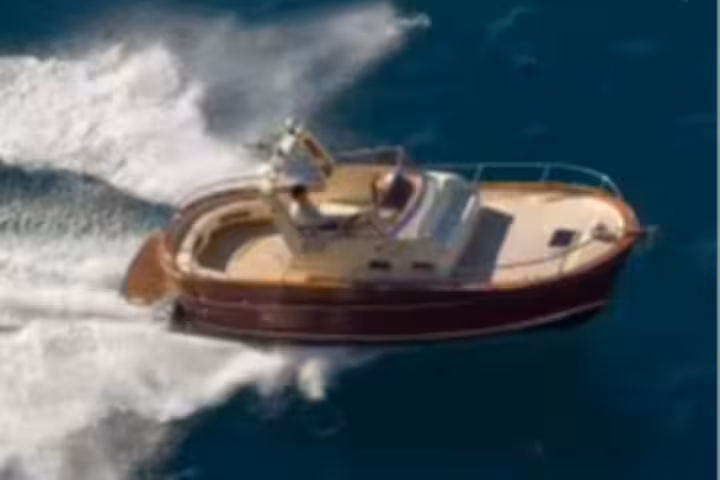 Cozy cabin with red bedding, wooden interiors and fruit platter on a private boat for Capri to Ischia transfer