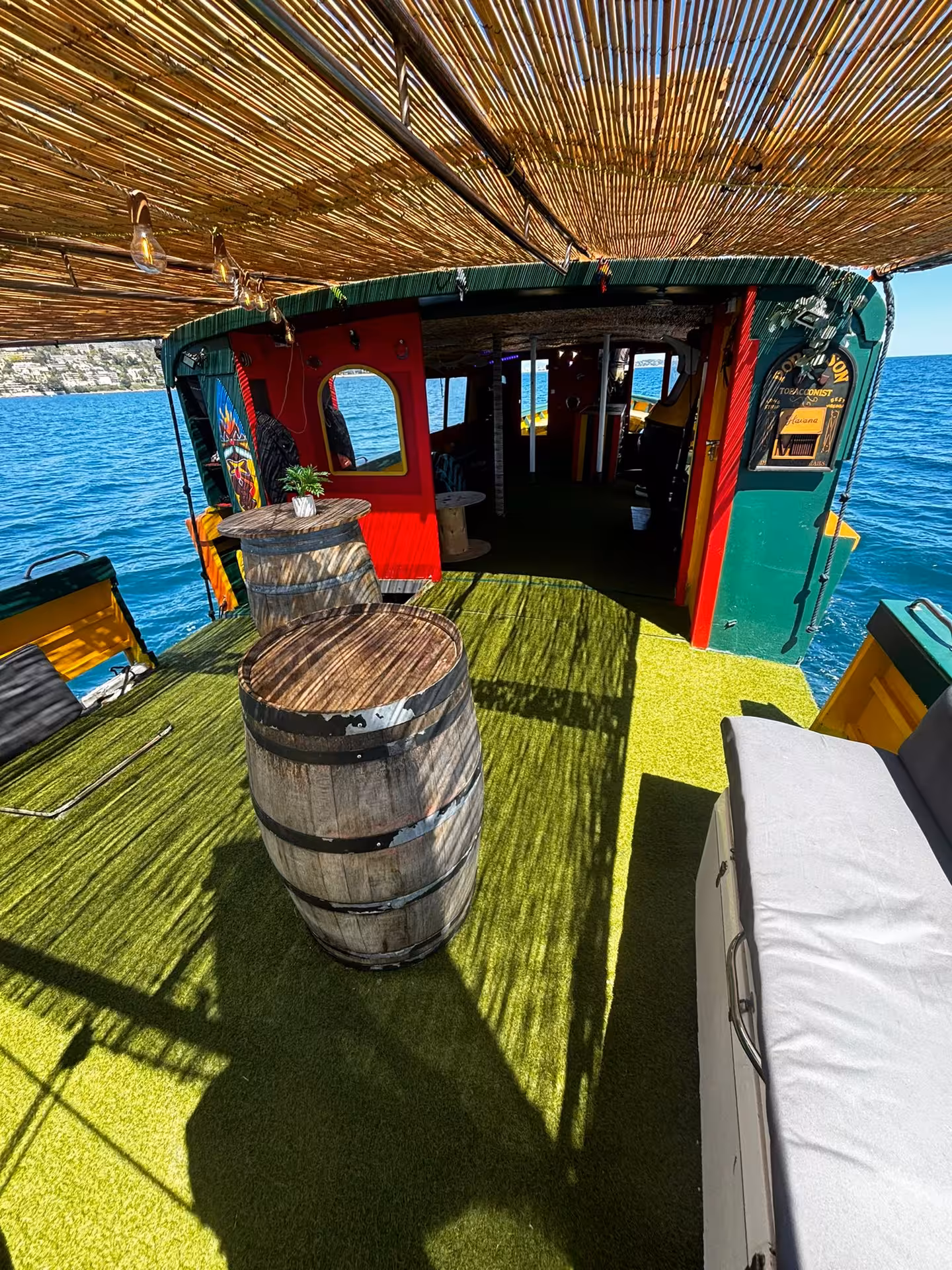Colorful private party boat deck with wooden barrels, green turf, and thatched roof on the French Riviera