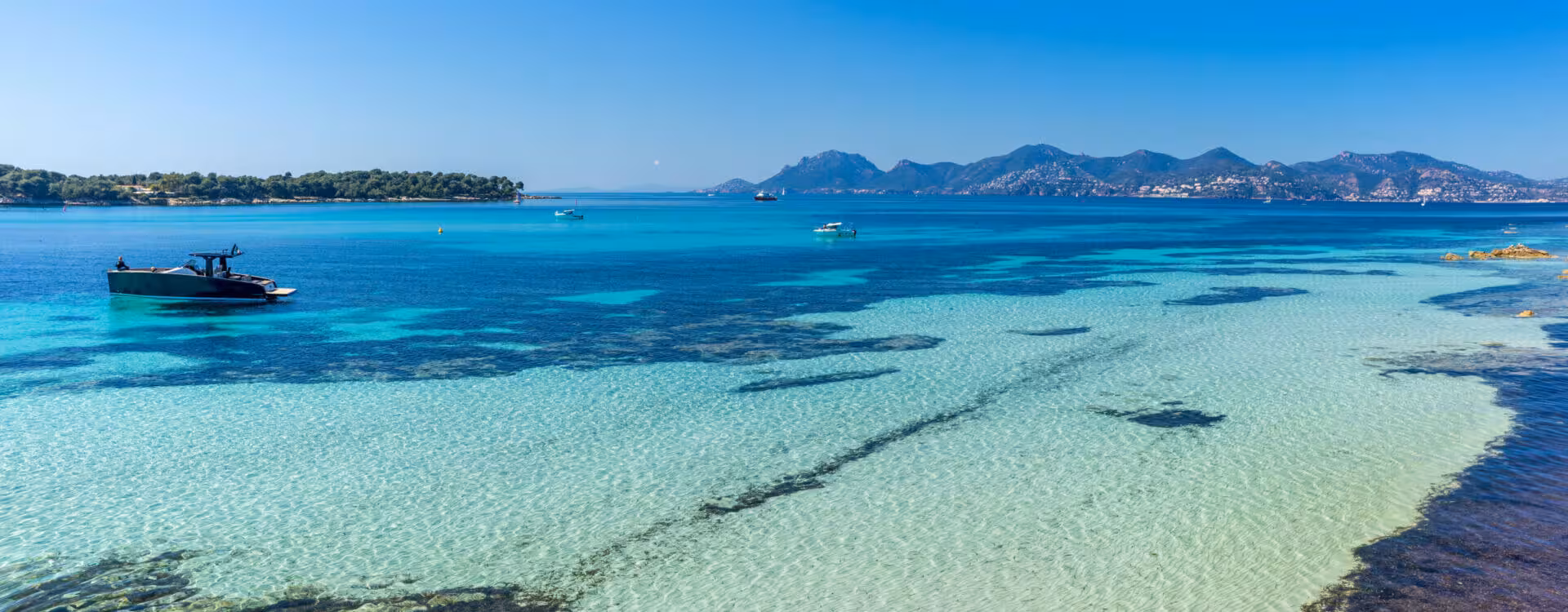 Crystal clear turquoise waters of the French Riviera with boats anchored near Cannes coastline and mountains