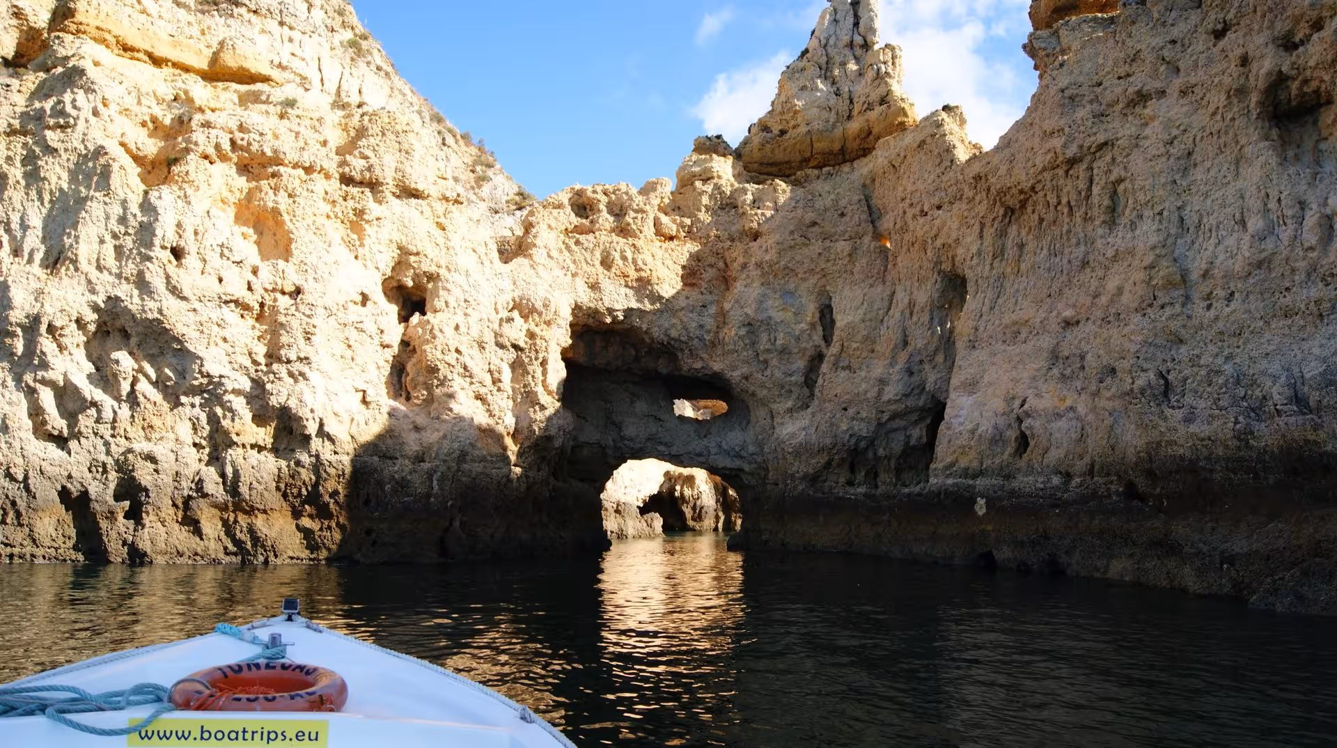 Private boat entering Ponta da Piedade grotto and rock arches in Lagos Algarve, calm water for swimming