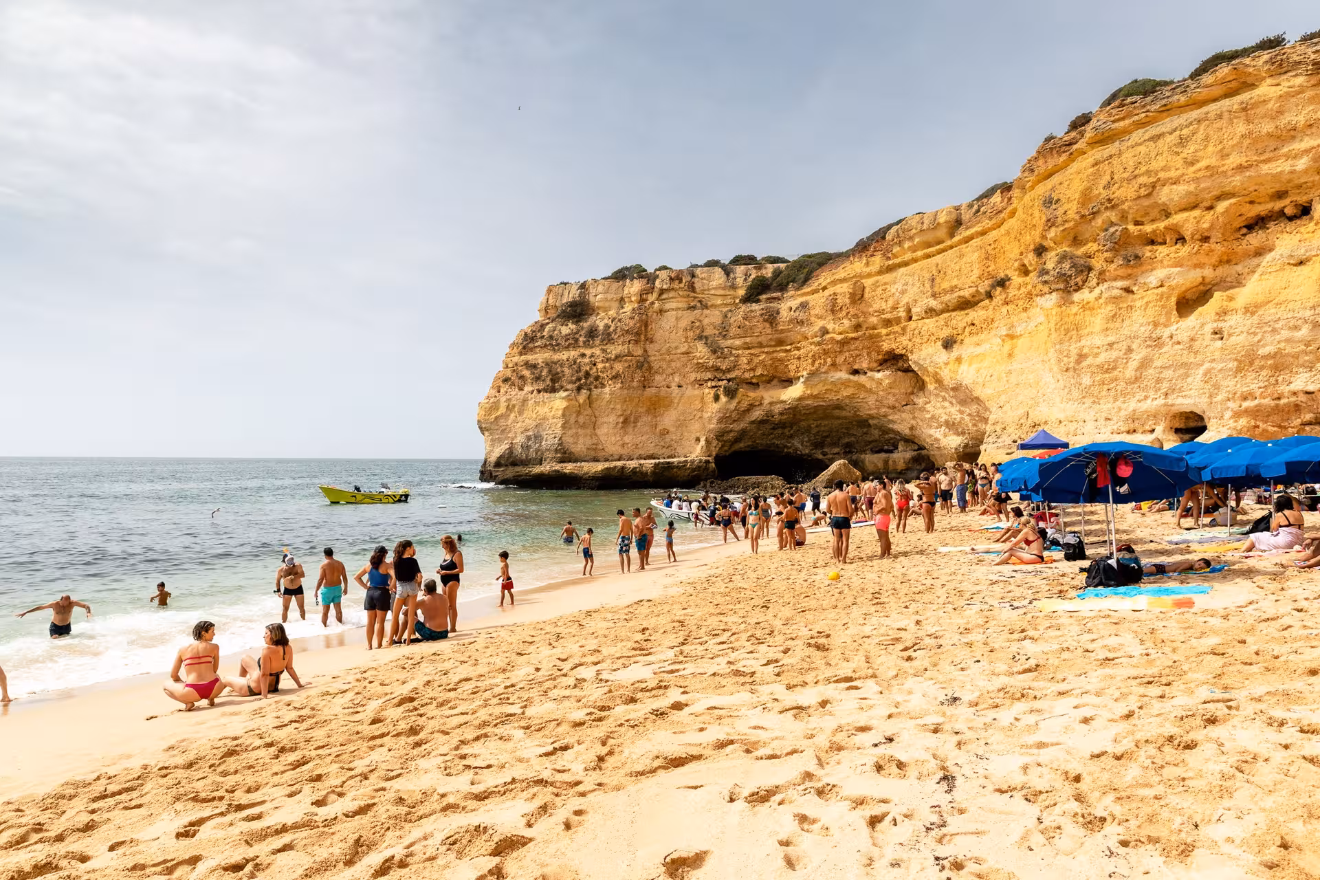 Tourists enjoy a sunny day on a picturesque Algarve beach with a private boat near stunning sea caves.