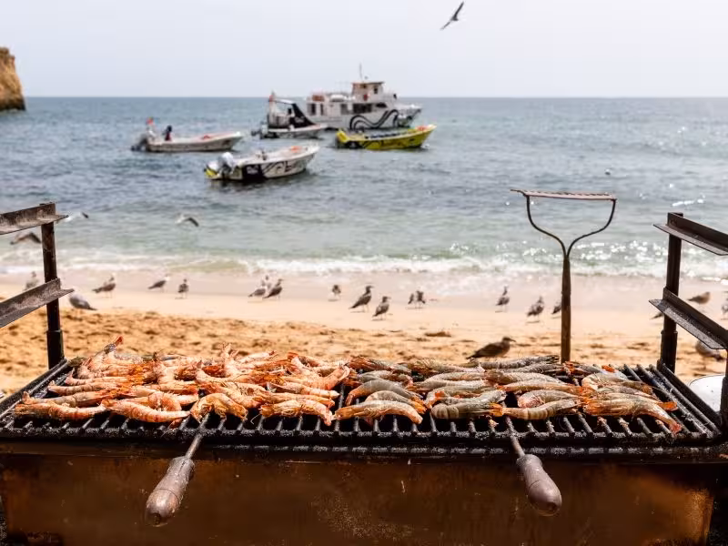 Grilled seafood on a beach with boats and seagulls, perfect for a private boat rental seaside dining experience.