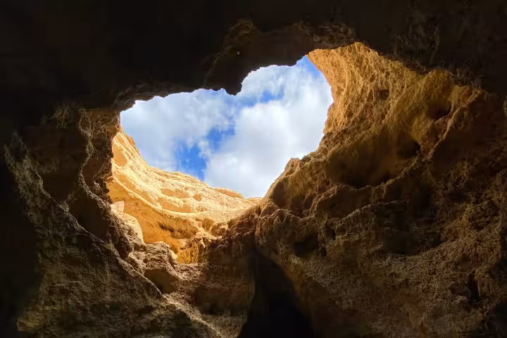 Small group on a private boat tour gliding into a dramatic Algarve sea cave, gazing up at the natural rock skylight and blue sky