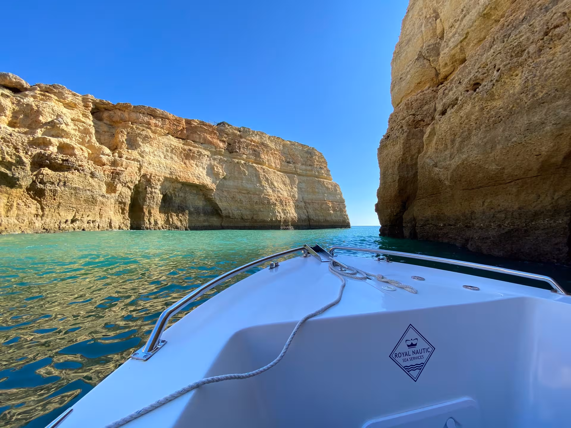 Small private boat gliding through turquoise water between Algarve sea cliffs on a sunny 4-hour coastal sightseeing tour