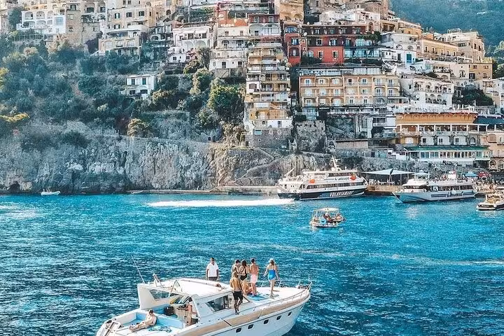 Tourists enjoy a private boat tour on the vibrant blue waters of the Amalfi Coast with Positano's colorful cliffside in view.