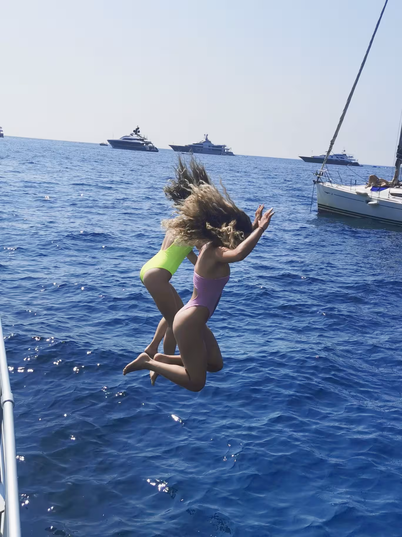 Two people joyfully jumping into the clear blue waters of Capri from a private boat tour, surrounded by yachts.