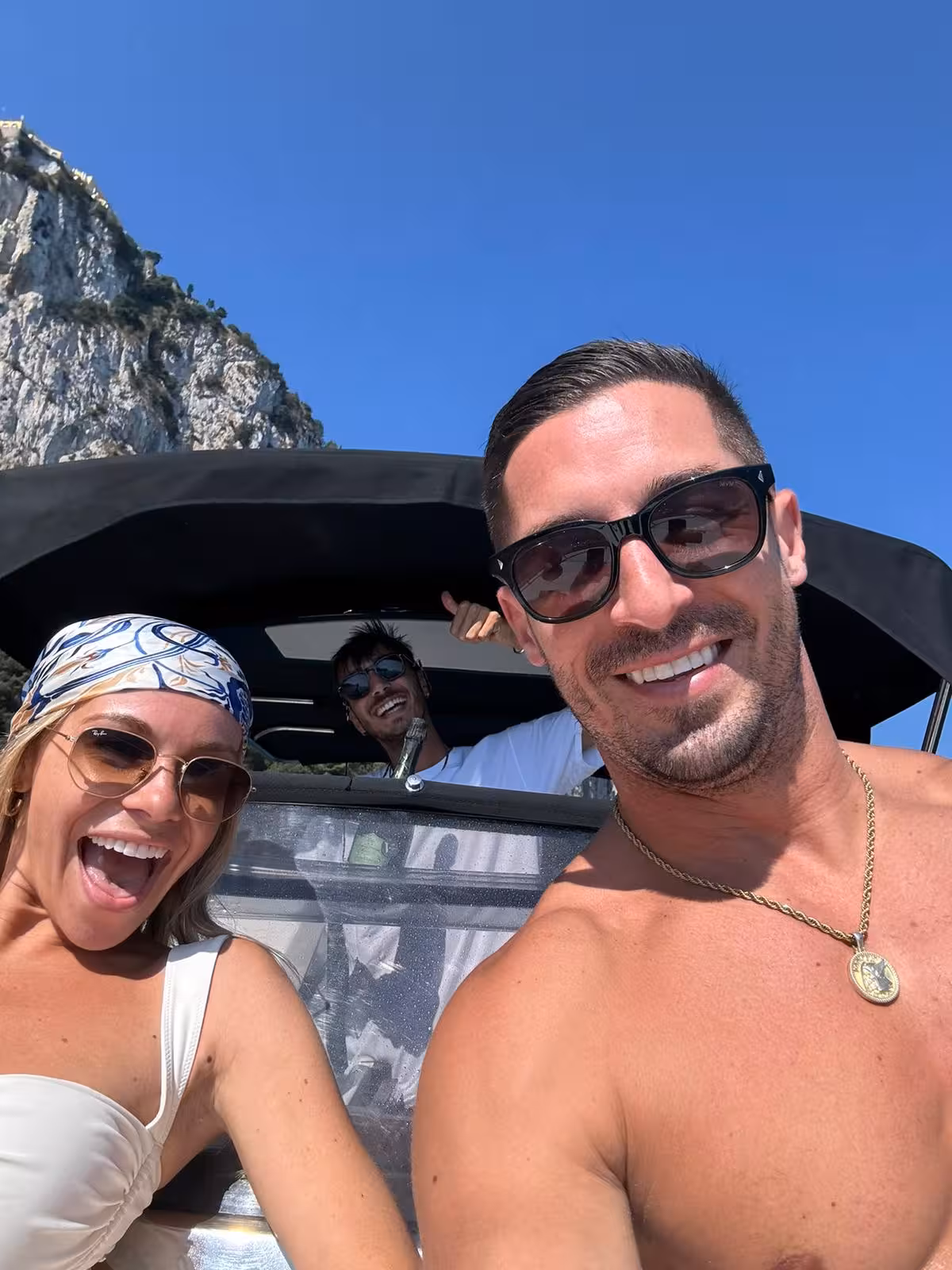 Smiling group enjoying a sunny day on a private boat tour to Capri, with stunning cliffs in the background.