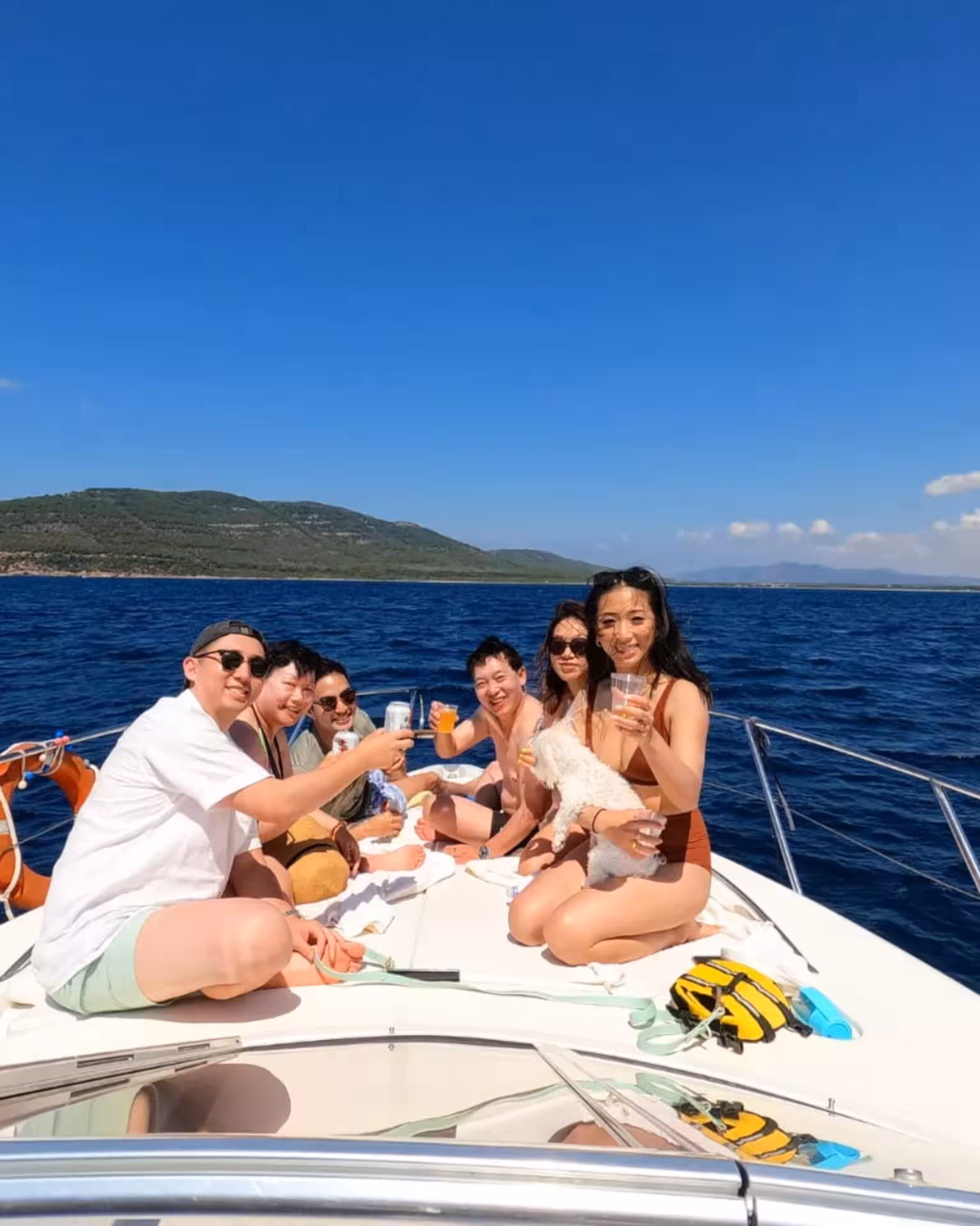 Group of friends celebrating on a private boat tour in the Gulf of Alghero, enjoying drinks and sunny views.