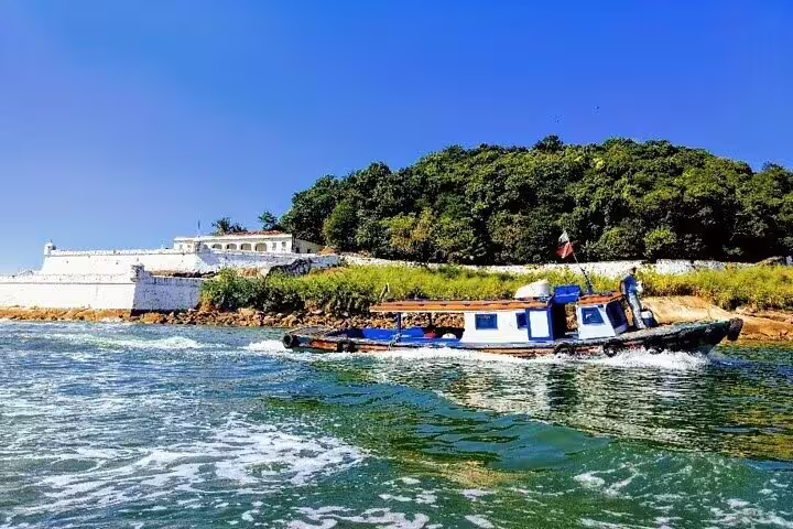 Small boat cruising near a historical fort in Santos, offering scenic views and cultural experiences on a private tour.