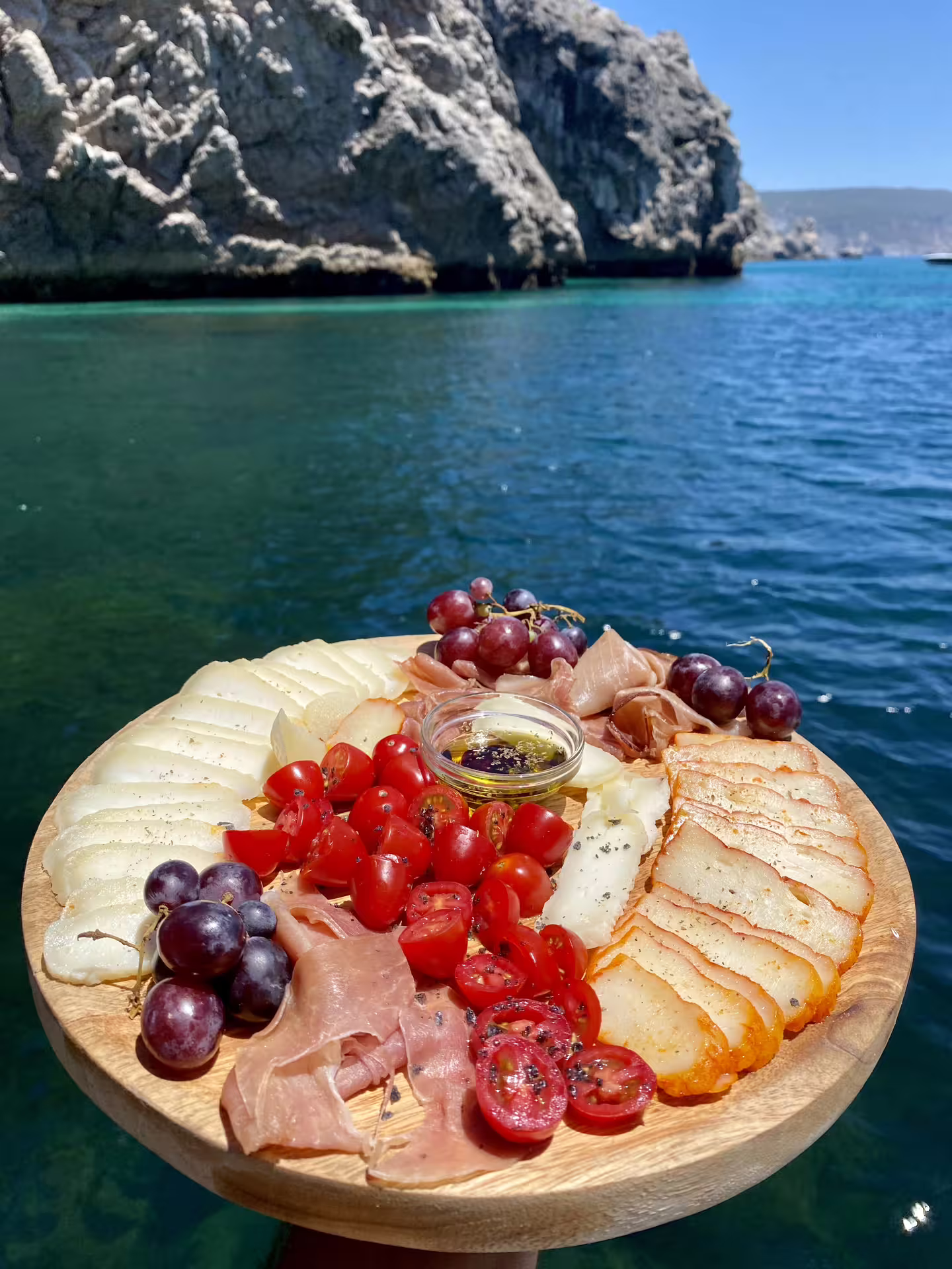 Charcuterie platter with cheese, grapes, and tomatoes on a private boat tour in stunning Sesimbra, Arrábida Park waters.