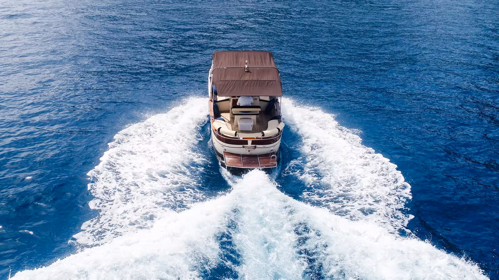 Private boat cruising through clear blue waters on a Sorrento to Amalfi tour, leaving a trail of white waves.