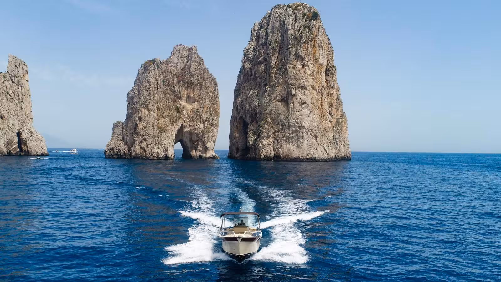Boat navigating between the iconic Faraglioni rocks on a private tour from Sorrento to Capri and Amalfi Coast.