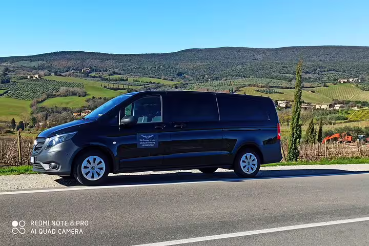 Luxury black minivan for private Brunello and Vino Nobile wine tour parked beside scenic Tuscan vineyards and hills