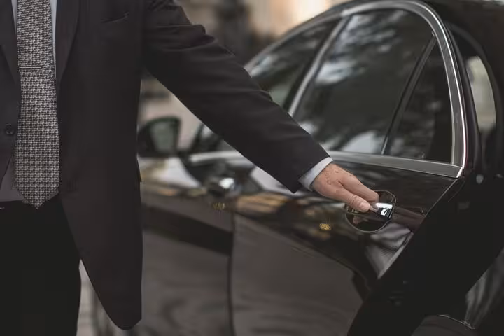 Professional chauffeur opening sedan door for private Cairo airport transfer from hotel, punctual pickup and comfort